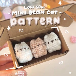 Puede incluir: Tres mini llaveros de gato de frijol en una caja de cartón. Los llaveros son blancos y beige, con detalles bordados en negro. La caja tiene el texto "Low sew - Mini Bean Cat - Pattern". Los llaveros están hechos a mano.