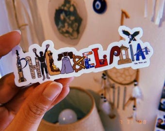 May include: A colorful sticker with the word "PHILADELPHIA" in various fonts and designs. The letters incorporate iconic city symbols like the Liberty Bell, a pretzel, and the Philadelphia skyline. An eagle graphic is at the top.
