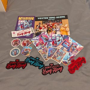 Puede incluir: Una colección de artículos de Hazbin Hotel Sing-Along que incluye un programa, una foto del elenco, un boleto, varias pegatinas circulares, impresiones artísticas rectangulares y cuatro parches bordados con el logotipo de Hazbin Hotel Sing-Along.