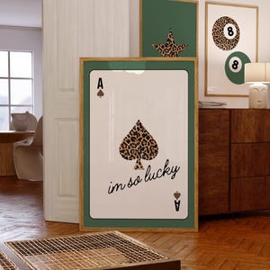 May include: A framed print of an ace of spades playing card with a leopard print design. The card says "im so lucky" in cursive writing.