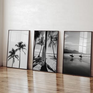 Può includere: Tre stampe d'arte da parete in bianco e nero con cornice. La stampa a sinistra mostra due palme su un cielo luminoso. La stampa centrale presenta una tavola da surf appoggiata a una palma su una spiaggia. La stampa a destra mostra due surfisti.