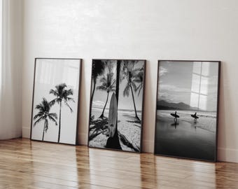 Può includere: Tre stampe d'arte da parete in bianco e nero con cornice. La stampa a sinistra mostra due palme su un cielo luminoso. La stampa centrale presenta una tavola da surf appoggiata a una palma su una spiaggia. La stampa a destra mostra due surfisti.