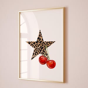 May include: A framed print with a white background featuring a large leopard print star with two red cherries hanging from the bottom point of the star.