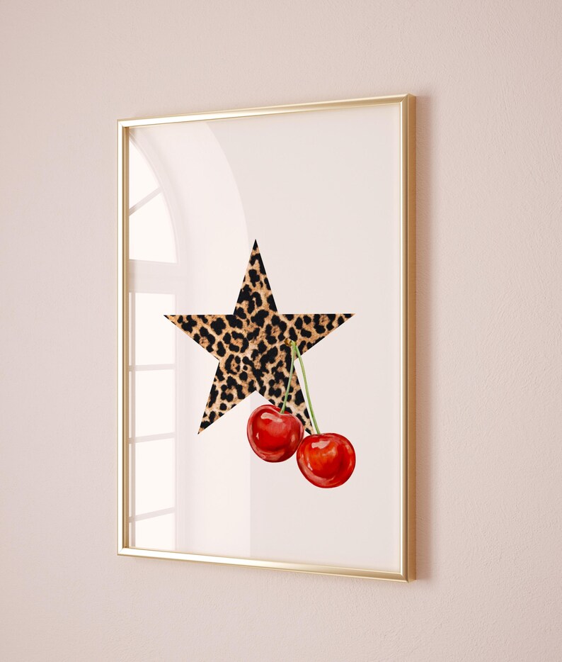 May include: A framed print with a white background featuring a large leopard print star with two red cherries hanging from the bottom point of the star.