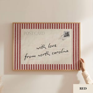 May include: A rectangular framed wall art piece featuring a vintage postcard design with a red and white vertical striped border. The center displays the text POST CARD, a squirrel stamp, and the handwritten script with love from north carolina.