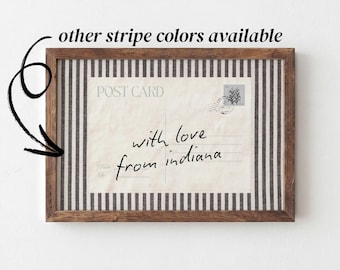 Puede incluir: Un marco de madera rectangular que contiene una inserción de tela con rayas verticales blancas y negras. El centro presenta un diseño de postal vintage con el texto "POST CARD" y "with love from indiana" escrito en letra negra.