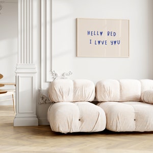 May include: A white couch with a light brown wood floor. A framed print with the text "Hello Bed I Love You" hangs on the wall behind the couch.