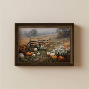 May include: A framed landscape painting depicting a rural field with a wooden fence, scattered orange and white pumpkins, and patches of white wildflowers under a misty sky. The artwork is enclosed in a dark brown, textured rectangular frame.