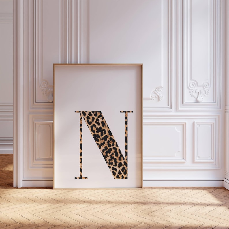 May include: A framed print featuring the letter "N" in a bold, serif font. The letter is filled with a leopard print pattern in shades of brown and black. The frame is a light brown color, and the background is a white wall.