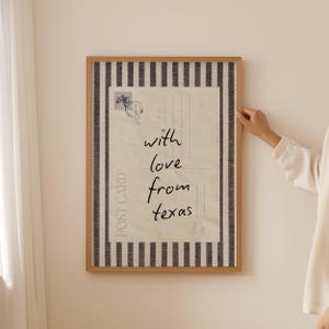 May include: A framed postcard print with the text "with love from texas" in a handwritten style. The print has a beige background with a postage stamp graphic and is framed with a wooden border and a black and white striped pattern.