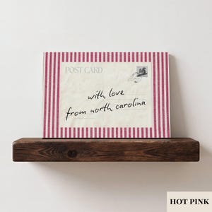May include: A rectangular postcard print featuring a cream-colored center with the text "POST CARD" and "with love from north carolina" in black script, accented by a small squirrel stamp and postmark, framed by a hot pink and white striped border.