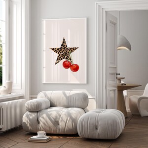 May include: A white framed print with a large, five-pointed star printed in a leopard print pattern. Two red cherries with green stems hang from the star.