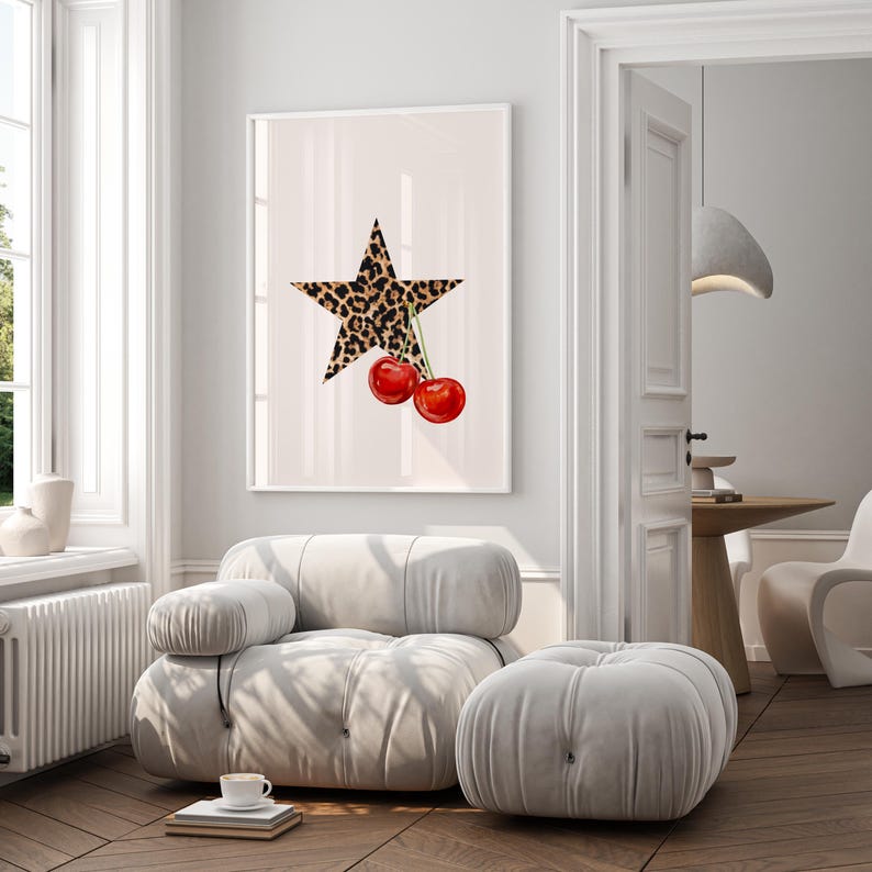 May include: A white framed print with a large, five-pointed star printed in a leopard print pattern. Two red cherries with green stems hang from the star.