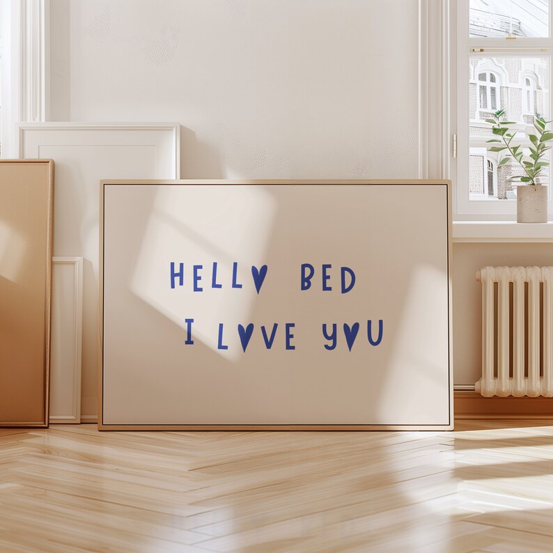 May include: A beige framed canvas with the text "Hello Bed I Love You" in blue lettering with blue heart symbols.
