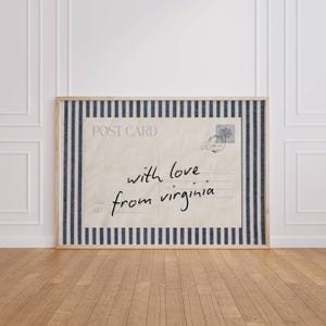 Könnte beinhalten: Ein rechteckiger Wandkunstdruck mit einem Vintage-Postkarten-Design, einem cremefarbenen Hintergrund, dunkelblauen und weißen vertikalen Streifen am Rand und dem handschriftlichen schwarzen Text "with love from virginia" in der Mitte.