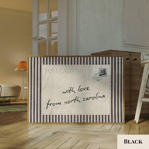 May include: A rectangular wall art print featuring a vintage postcard design with a cream-colored center and black and white vertical stripes on the borders. The text reads POST CARD and with love from north carolina in black cursive script.