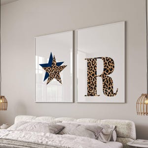 May include: Two framed wall art prints. One features a blue star over a leopard print star. The other print displays the letter "R" in a leopard print pattern. The prints are displayed above a bed with white bedding.