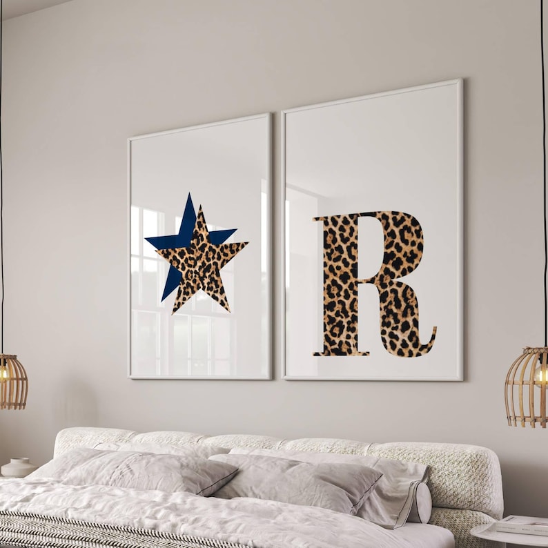 May include: Two framed wall art prints. One features a blue star over a leopard print star. The other print displays the letter "R" in a leopard print pattern. The prints are displayed above a bed with white bedding.