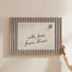 Può includere: Stampa di cartolina incorniciata con un'estetica vintage. Il design presenta una cartolina color crema con le parole "with love from illinois" in scrittura manoscritta. La cornice ha un bordo a righe.