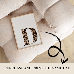 May include: A framed print featuring the letter "D" in a leopard print design. The print has a white background and a light wooden frame. The text "PURCHASE AND PRINT THE SAME DAY" is at the bottom of the image.