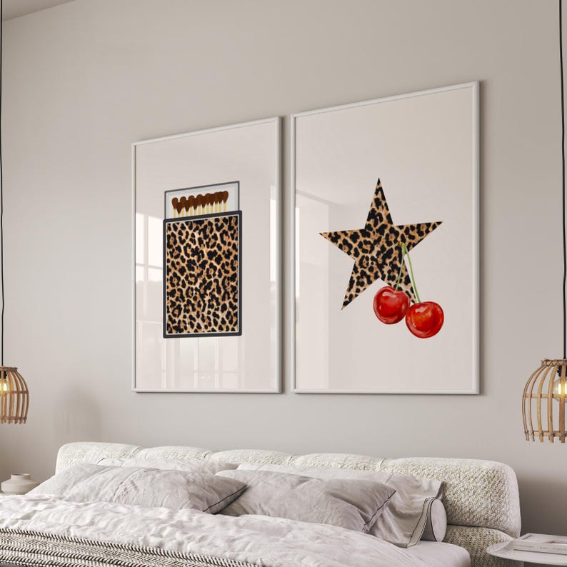 May include: Two framed prints with a leopard print design. The print on the left shows a box of matches with a leopard print design. The print on the right shows a star with a leopard print design and two red cherries.