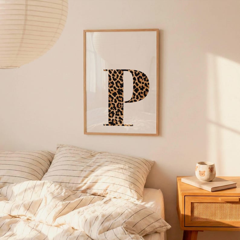 May include: A framed print featuring the letter "P" in a bold, leopard print design. The letter is centered on a cream-colored background, encased in a light wood frame. The artwork adds a touch of wild style to any room.