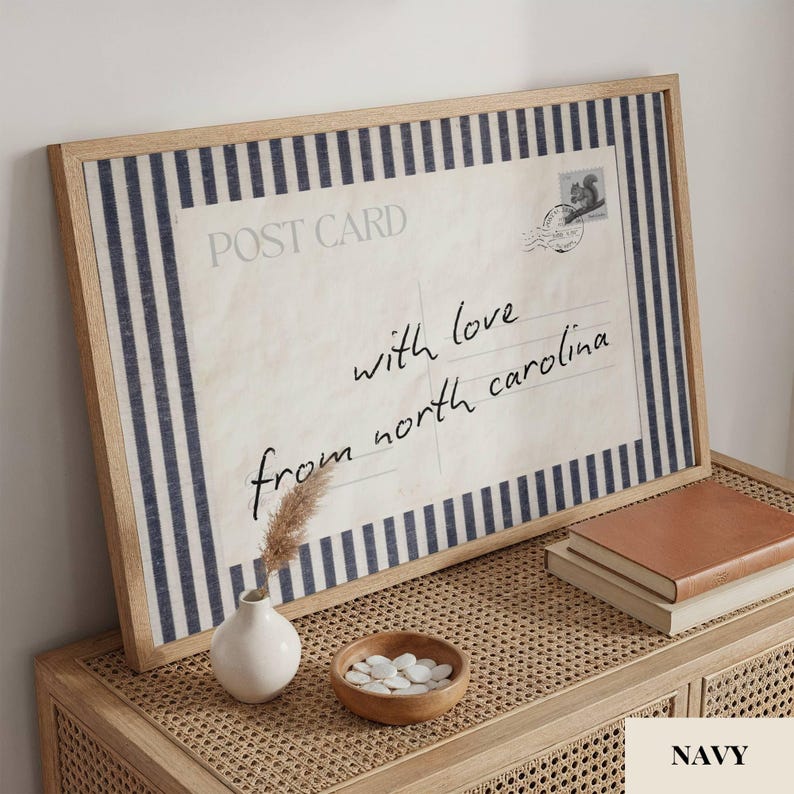May include: A framed rectangular print featuring a vintage postcard design with navy blue and white vertical stripes. The text reads POST CARD and with love from north carolina, accompanied by a small stamp illustration and a circular postmark.