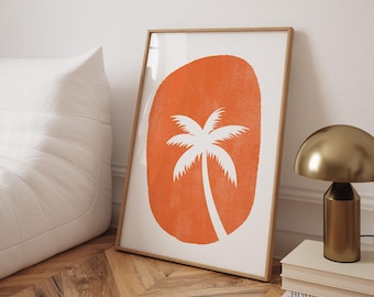 Op de afbeelding: Ingelijste kunstdruk met een wit palmboom silhouet op een oranje ovaal. De print staat in een lichtbruine houten lijst, leunend tegen een witte muur. Het kunstwerk wordt tentoongesteld op een houten vloer.