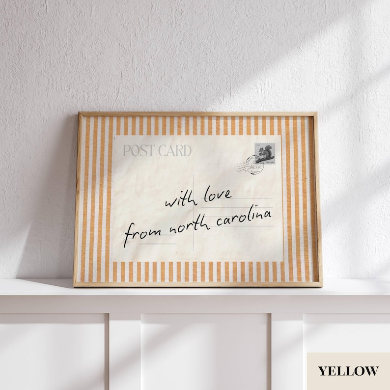 May include: A rectangular framed print featuring a vintage-style postcard design with the text "POST CARD" and "with love from north carolina" in black script. The frame has a light orange and white vertical striped pattern border.