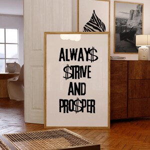 Puede incluir: Una impresión artística enmarcada con las palabras "ALWAYS STRIVE AND PROSPER" en letras negras en negrita. El símbolo del dólar está incorporado en la letra. La impresión está en una habitación con otras obras de arte enmarcadas y muebles de madera.