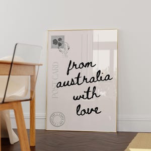 May include: A framed print resembling a postcard, featuring the text "from australia with love" in a handwritten style. The print includes a postage stamp and a circular seal, all in black against a cream background. The frame is gold.