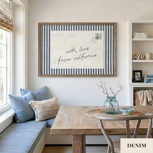 May include: A rectangular wall art piece featuring a vintage postcard design with the text "with love from california" centered on a cream background, framed by a blue and white vertical striped border in a brown wooden frame.