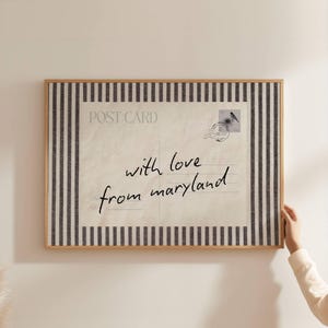 May include: A rectangular wall art print featuring a vintage postcard design with the text "with love from maryland" in black script. The postcard is framed by a vertical black and white striped border and enclosed in a light wood frame.