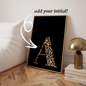 Könnte beinhalten: Ein gerahmter Kunstdruck mit dem Buchstaben "A" in einem Leopardenmuster auf schwarzem Hintergrund. Der Text "add your initial!" befindet sich über dem Rahmen. Der Rahmen ist hellbraun.