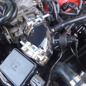 May include: Close-up of a black engine intake pipe with a silver clamp and a black warning label that reads "CAUTION  DANGER 2,000  WARNING".