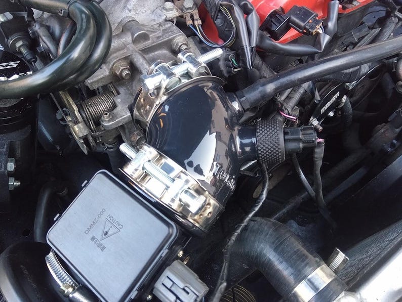 May include: Close-up of a black engine intake pipe with a silver clamp and a black warning label that reads "CAUTION  DANGER 2,000  WARNING".