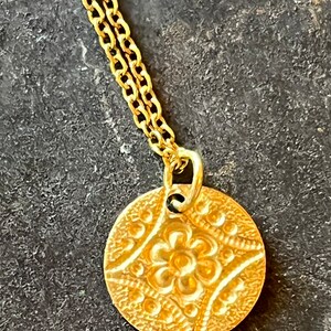 May include: A gold chain necklace with a round pendant featuring a detailed floral design.