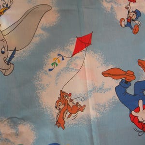 May include: A light blue fabric featuring cartoon characters Dumbo, Donald Duck, Jiminy Cricket, Chip and Dale, and Goofy. Dumbo is flying, Chip and Dale are flying a kite, and Goofy is falling with a balloon. The fabric has a sky and cloud background.