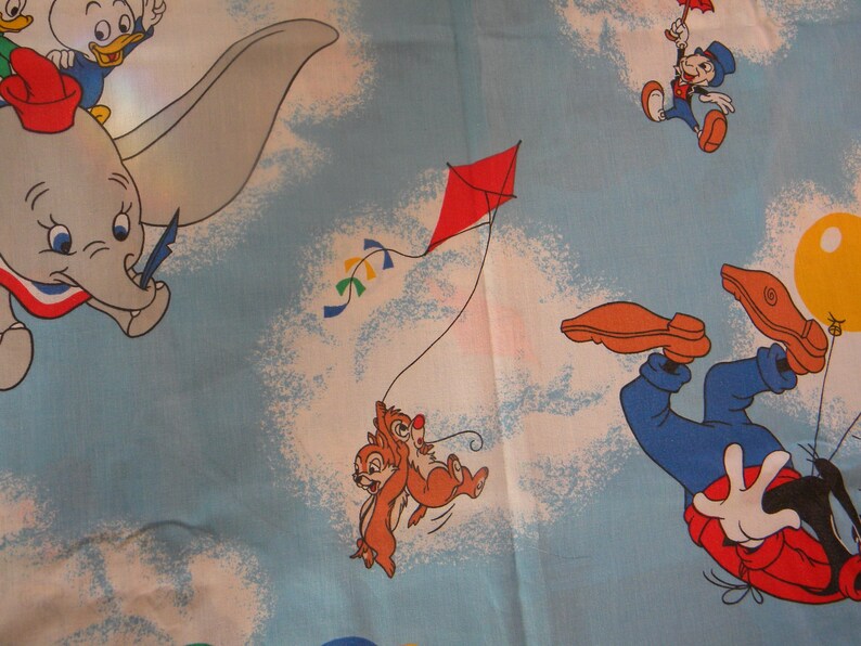 May include: A light blue fabric featuring cartoon characters Dumbo, Donald Duck, Jiminy Cricket, Chip and Dale, and Goofy. Dumbo is flying, Chip and Dale are flying a kite, and Goofy is falling with a balloon. The fabric has a sky and cloud background.