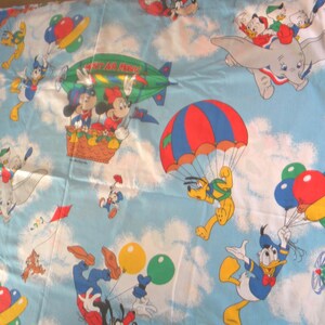 May include: Light blue fabric featuring a repeating pattern of Disney characters in the sky. Mickey and Minnie Mouse are in a basket, Pluto is parachuting, and Donald Duck is holding balloons. Dumbo and other characters are also present.