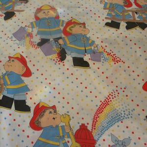 May include: White sheet featuring a repeating pattern of cartoon firefighters in blue uniforms and red helmets. The firefighters are holding buckets and tools, with colourful confetti scattered across the surface. The sheet has a vintage, playful aesthetic.