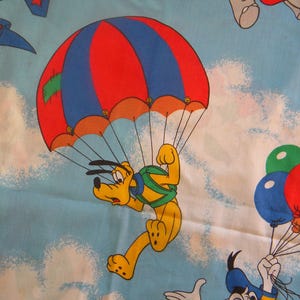 May include: A cartoon illustration of Pluto parachuting from a red and blue parachute against a light blue sky with white clouds. Other cartoon characters and balloons are also visible.