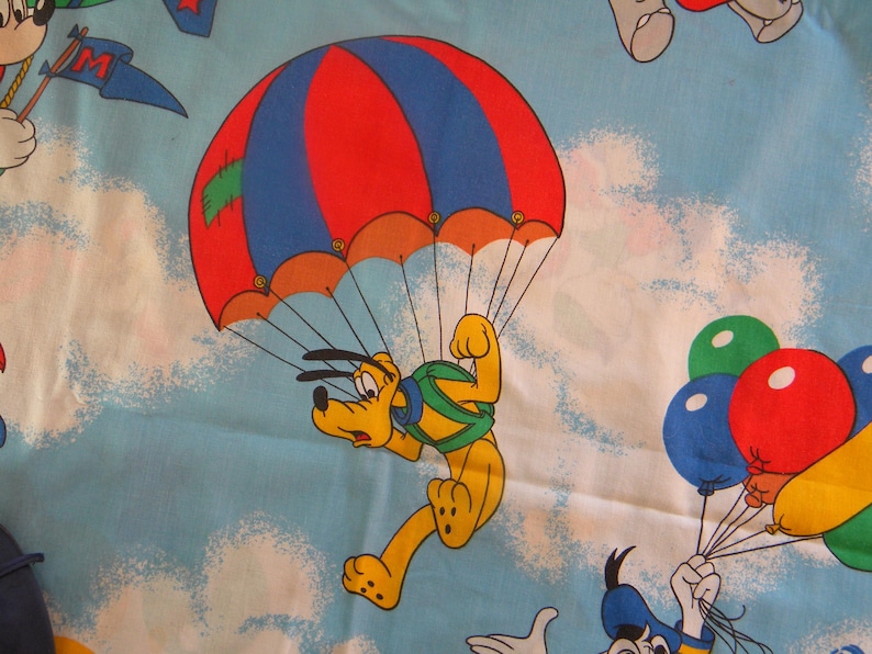 May include: A cartoon illustration of Pluto parachuting from a red and blue parachute against a light blue sky with white clouds. Other cartoon characters and balloons are also visible.