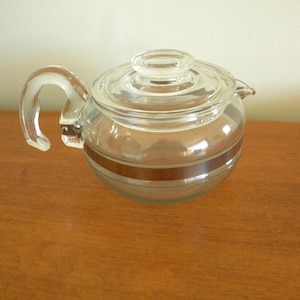 May include: A clear glass teapot with a brown band around the middle. The teapot has a lid and a handle.