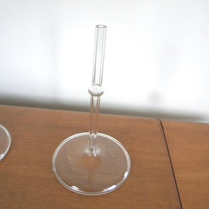 May include: Clear glass stemware with a round base and a slender stem. The stem has a small, round detail near the top. The glass is transparent, allowing light to pass through. The stemware is placed on a wooden surface.