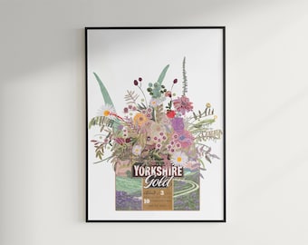 Può includere: Una stampa d'arte incorniciata raffigurante un colorato bouquet di fiori di campo e vegetazione che emerge da una scatola di tè Yorkshire Gold. La scatola mostra il testo Yorkshire Gold, Blend of 3 e 10, su un'illustrazione di colline.