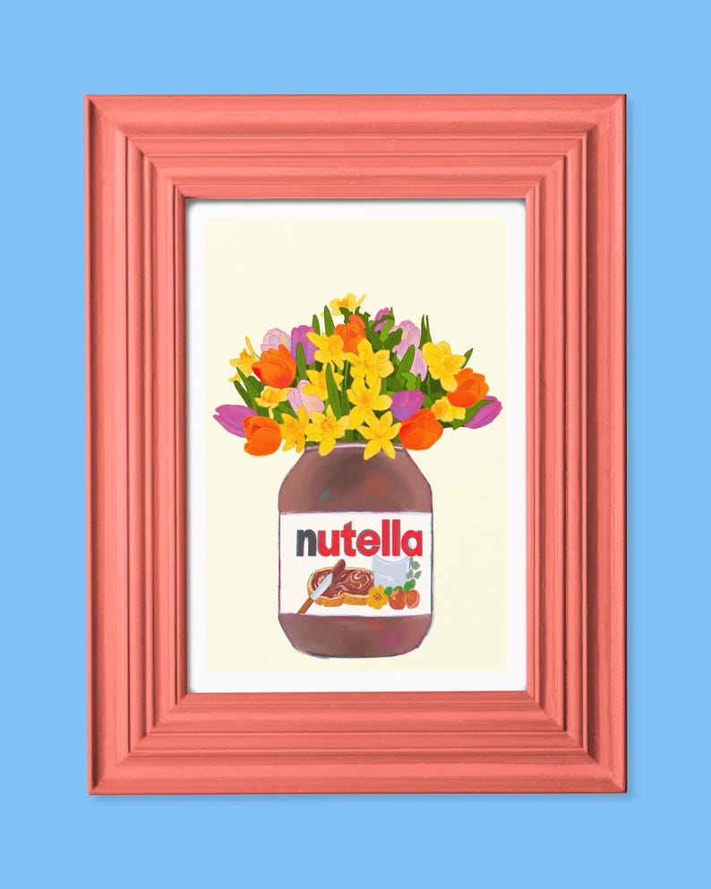May include: A framed art print featuring a jar of Nutella filled with a bouquet of colorful flowers. The flowers include orange tulips, yellow daffodils, and purple flowers. The frame is a coral color, set against a light blue background.