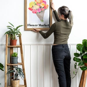 May include: A framed print featuring a watercolor illustration of a bouquet of flowers in shades of yellow, pink, and orange. The print is labeled "Flower Market Botanical Collection". The frame is a light brown color.