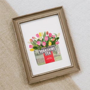 May include: A framed watercolor print featuring a bouquet of pink and yellow tulips arranged in a Yorkshire Tea box. The box has the words "Yorkshire Tea" printed on it, with the phrase "Let's have a proper brew" below.