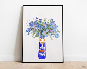 May include: A framed art print featuring a blue Matey bubble bath bottle used as a vase, filled with a vibrant bouquet of blue and pink forget-me-not flowers. The bottle displays the text up to 20 baths and Matey bubble bath in orange and white.